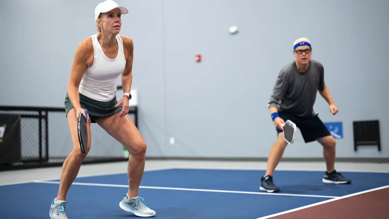 Co-ed doubles players in ready positions on an indoor pickleball court